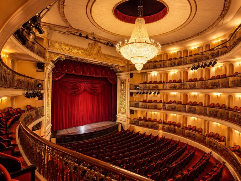 Palco com cortina vermelha, lustre de cristal e camarotes de um teatro histórico
