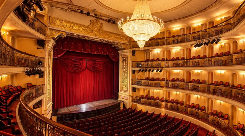 Palco com cortina vermelha, lustre de cristal e camarotes de um teatro histórico